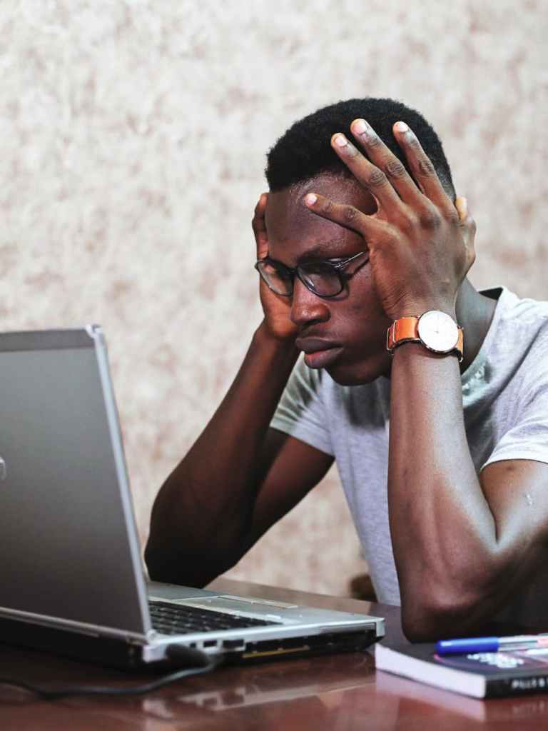 Frustrated man with head in hands in front of a laptop